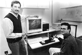 Mandayam Srinivasan, director of MIT's Touch Lab, stands next to a monitor displaying a virtual rendition of a liver. Research Scientist Cagatay Basdogan is manipulating the liver with a robotic device that translates the touch and feel of virtual objects to the user. The work could lead to surgical training based on virtual reality.