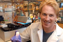 MIT research associate Dan Anderson holds a slide patterned with some 1,700 spots of biomaterial upon which he grows human embryonic stem cells. The machine behind him is the robot key to patterning and analyzing the slide.