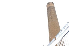 Inventor Isaac Berzin, left, converses with Peter Cooper, director  of  utilities in MIT's Department of Facilities, atop MIT's cogeneration plant. Berzin's company, GreenFuel, is installing bioreactors consisting in part of  temperature-controlled tubes, at right, which will hold algae through which waste gases will pass.