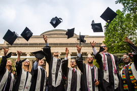 Row of students in graduation regalia throwing their mortarboards up in the air