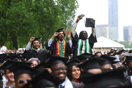 Three graduating seniors stand up in the crowd, cheering