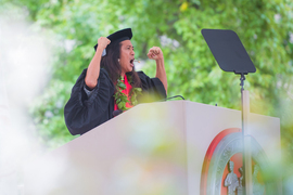 Kealoah at the podium, wearing graduation regalia and a green-leaf lei