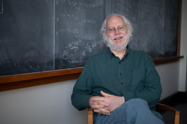 Peter Shor sits in a chair in front of a chalkboard