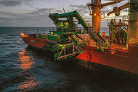 Gigantic arms of an orange and green ship are about to place the smaller green Patania II in the ocean.