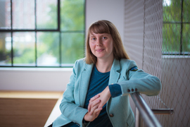 Skylar Larsen sits indoors, arm on railing, with windows and a wire wall in background