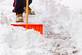 A person in boots shovels snow on a sidewalk.