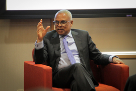 Neves sits on a red armchair and speaks to the audience while gesturing with his hands.