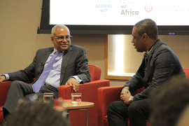 Grunitzky, right, and Neves are in conversation while seated in front of an audience. A slideshow is glimpsed in the background.