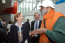 Inside the Stata Center, Susan Hockfield smiles while listening to Mel King on right, with Steve Lerman in center. People mingle in background.