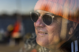 Behind a window, Charles smiles while wearing sunglasses, and we see the river reflection on the window.