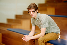 Tzouanas sits on wooden bleachers and leans forward with hands clasped.