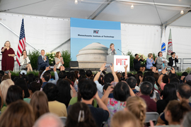 A crowd takes photos and claps, as Kornbluth smiles and claps onstage. Other members of community are on stage clapping.