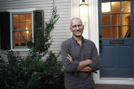 Moungi Bawendi, smiling with arms folded, in front of his home. 