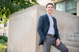 Nathaniel Hendren smiles and stands on the steps outside Walker Memorial. In background, etched in stone, are the words, “50 Memorial Drive.”