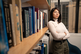 Nicole McGaa crosses her arm while next to a bookshelf, and the bookshelf blurs as it gets near the camera.