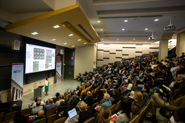 A packed auditorium listens as Paula Hammond presents her research using a slide show.