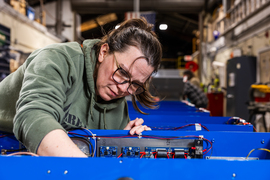 A person inspects parts on blue pieces of equipment.