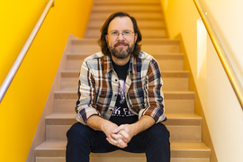 Mark Harnett sits on stairs, with yellow walls on the sides.