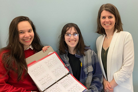 Ananda Santos, Casey Fienberg, and Anna Frebel pose for a group photo while holding a binder with lots of charts.