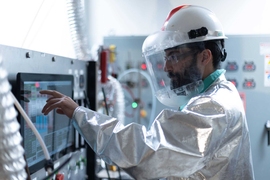 Tomás Villalón wears a clean suit and helmet while using a touch screen in the clean room.