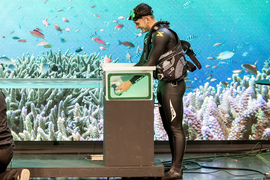 A scuba diver puts goggles in an aquarium while on stage.