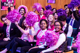 A group of people dressed in pink and with pom-poms cheer in the audience