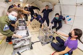 People floating in zero gravity with multiple experiment tanks